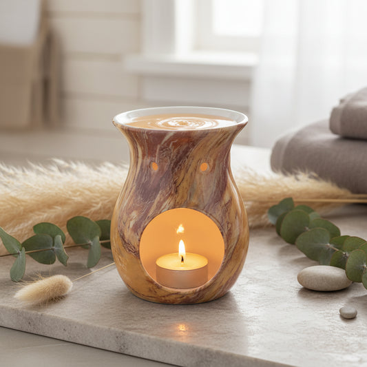 Decorative wax melt burner with a marble effect pattern in orange and russet tones with a lit tealight sitting on a marble type countertop