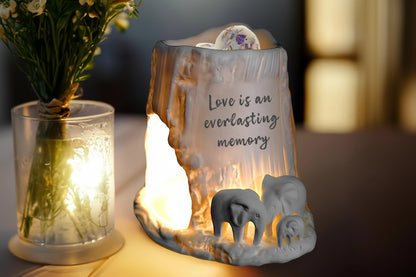 Elephant tealight burner with decorative elephants and text, surrounded by a soft glow.