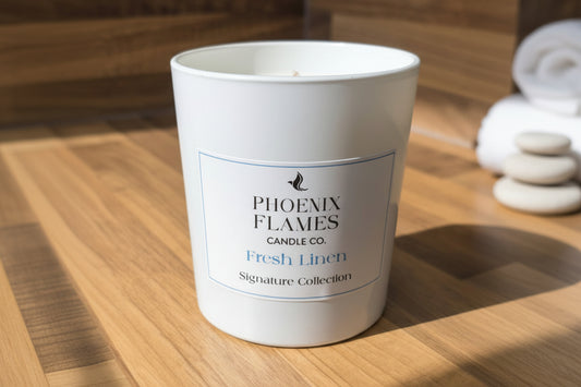 Candle labeled 'Phoenix Flames Candle Co, Fresh Linen' on a wooden surface