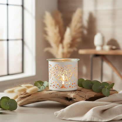 Decorative candle holder with a lit candle on a wooden surface, surrounded by greenery and a blurred indoor background.