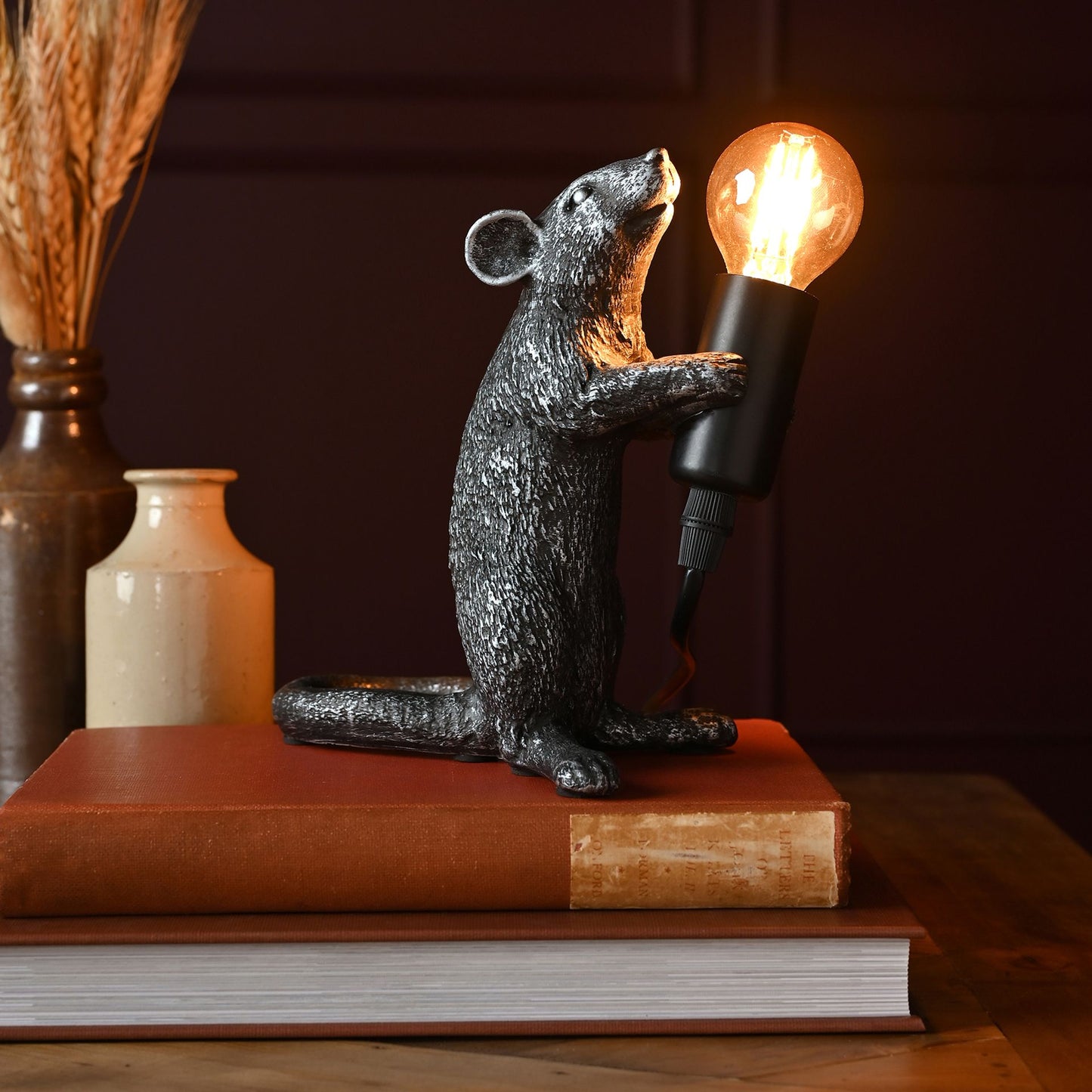 Decorative lamp shaped like a mouse holding a light bulb on top of books.