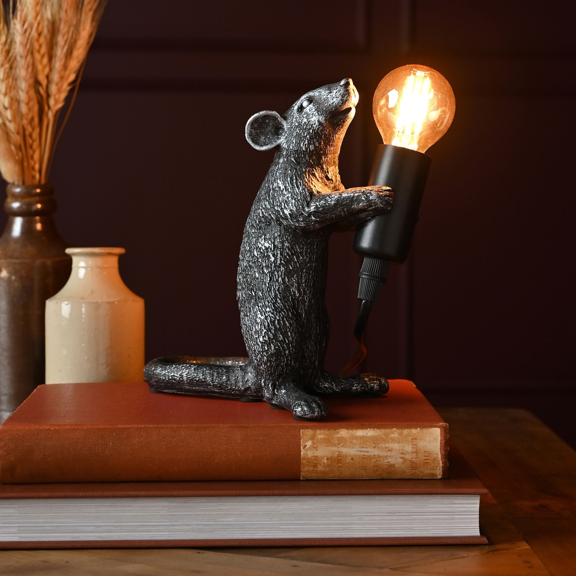 Decorative lamp shaped like a mouse holding a light bulb on top of books.