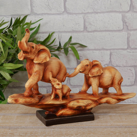 Wooden effect cast resin figurine of two elephants and a calf on a natural wood base against a white brick wall.