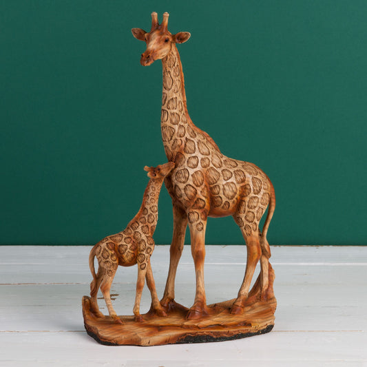 Wood effect resin figurine of two giraffes on a wood effect resin base against a green background