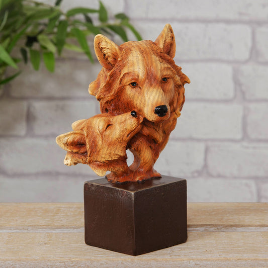 Wooden effect resin figurine of a wolf and cub on a square base with a plant and brick wall in the background.